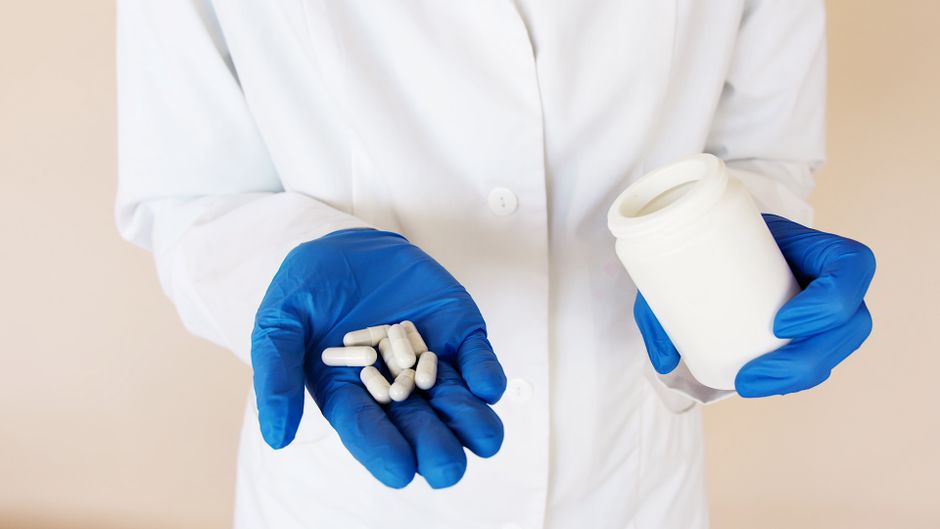 A gloved hand holding a small pile of capsules next to a pill bottle