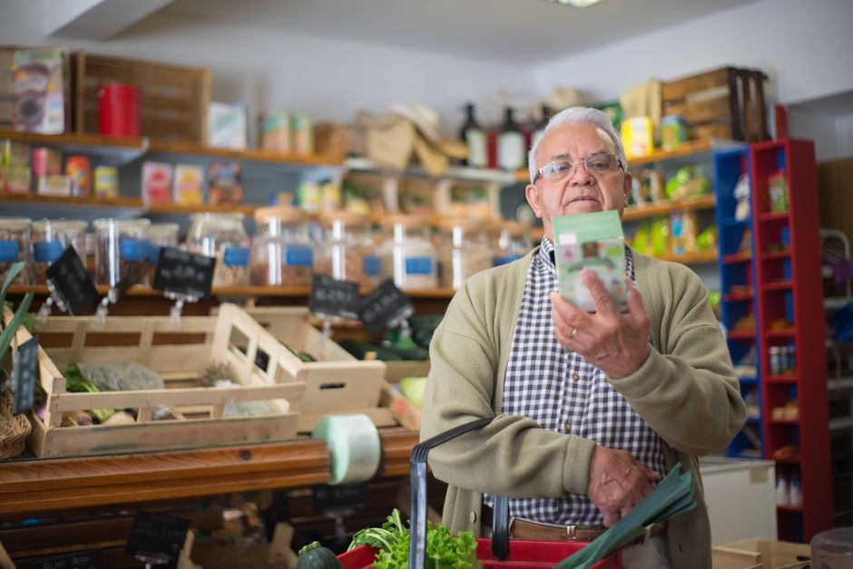 An older man in a grocery store reading the label on a product he is holding