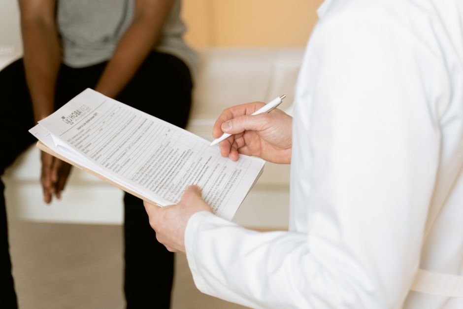 A doctor reviewing a clipboard form while consulting with a seated patient