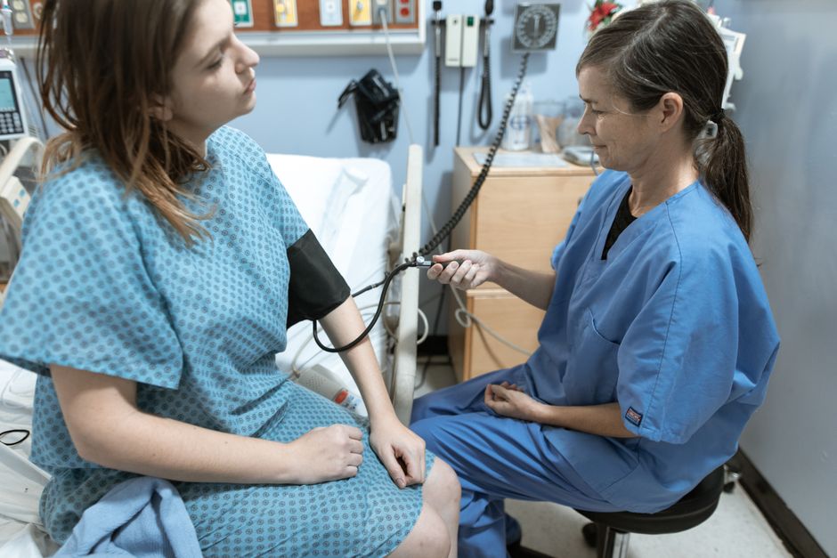 A nurse checking a seated patient's blood pressure in a clinical room